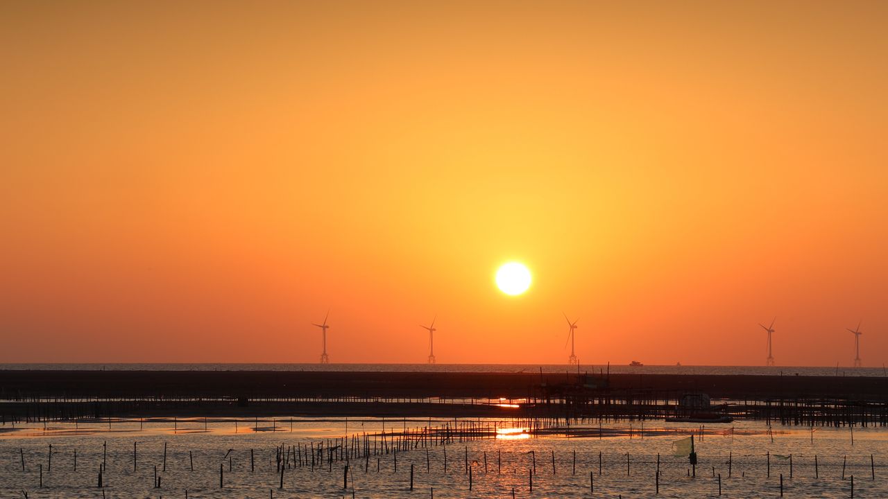 Home A beautiful ocean sunset with wind turbines against an orange sky.